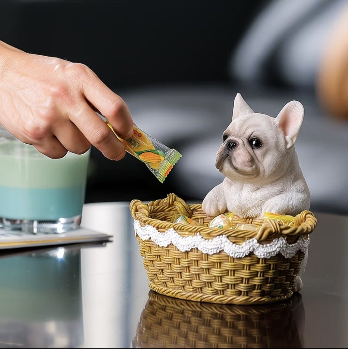 Frenchie in basket resin figurine on a table, hand placing a snack
