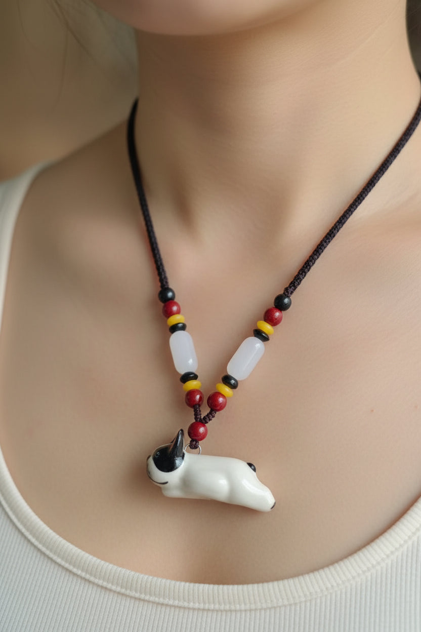 Pied Frenchie ceramic necklace on a beaded cord, held in a hand